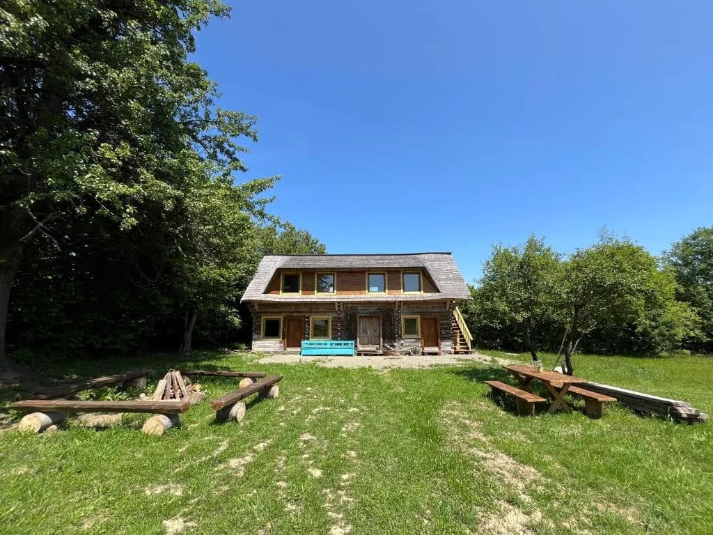 Casa de lemn din Breb, cu bancă turcoaz și masă de picnic în livadă
