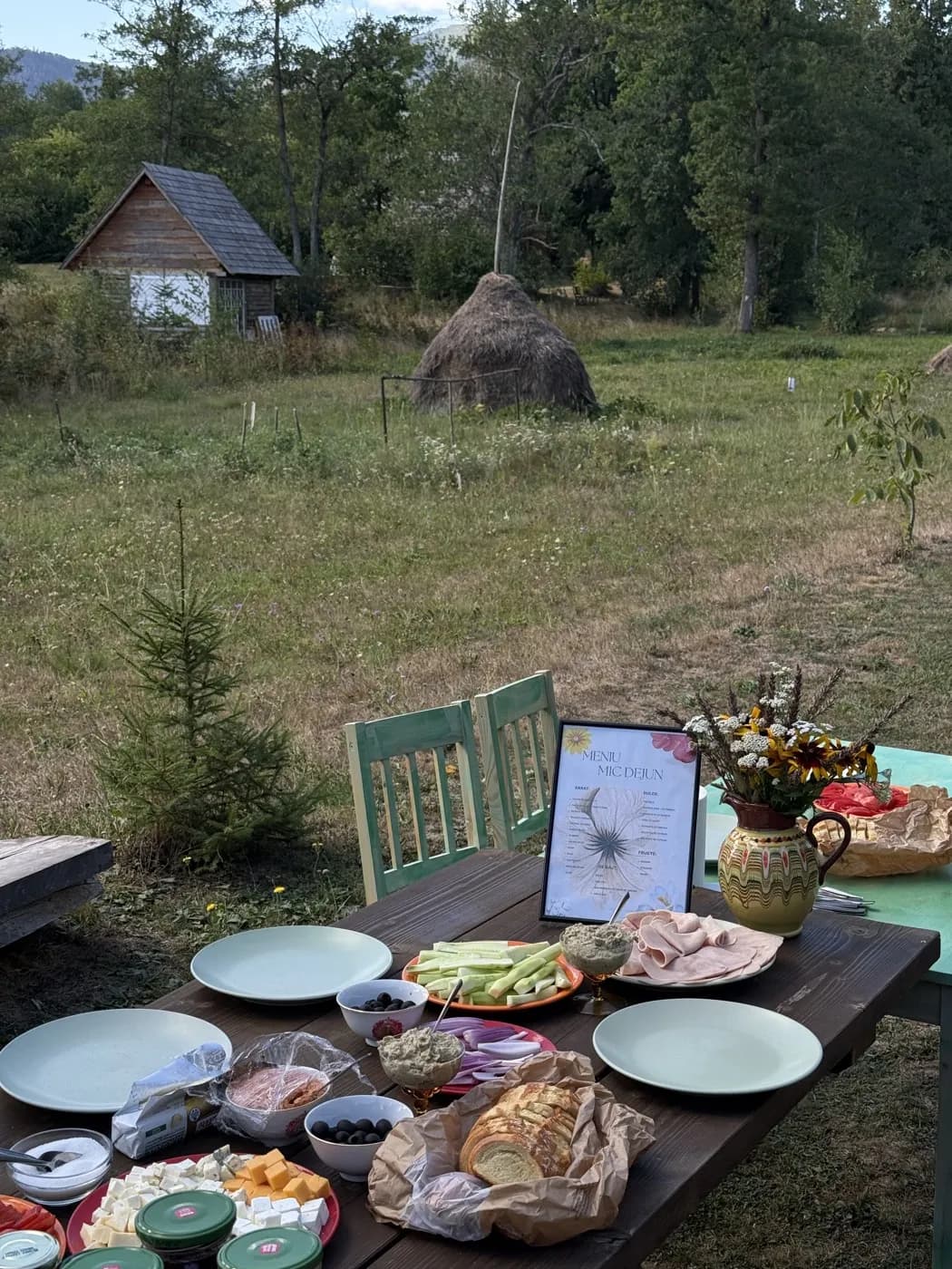 Masa întinsă afară, în livadă, cu o căpiță de fân în spate