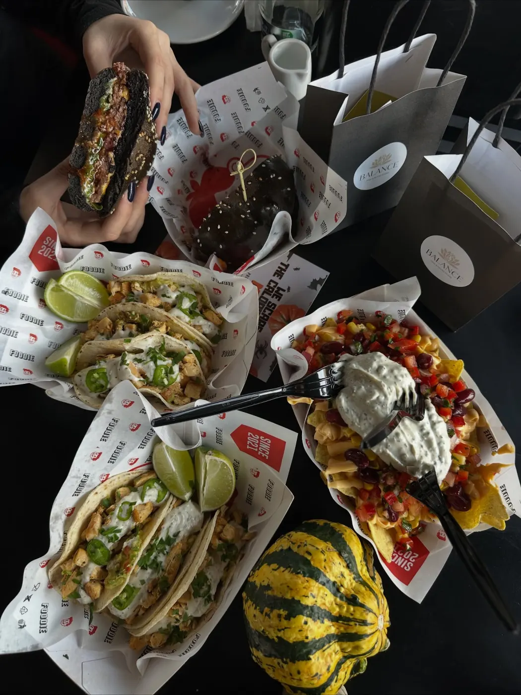 Tacos, burgerul negru și nachos pe masă, cu pungile Balance și un dovleac dungat